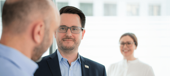 Zwei Beschäftigte im Gespräch. Eine Kollegin steht lächelnd im Hintergrund.