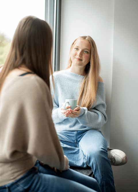 Auszubildende sitzt auf Fensterbank mit Kaffeetasse in der Hand